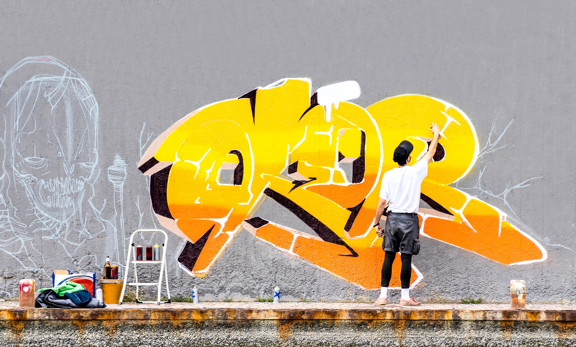 Street artist painting colored graffiti on public space wall